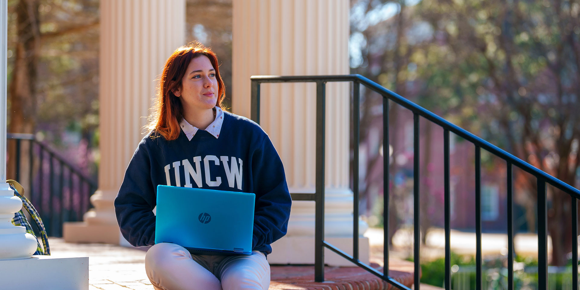A student sits on steps in a UNCW sweatshirt