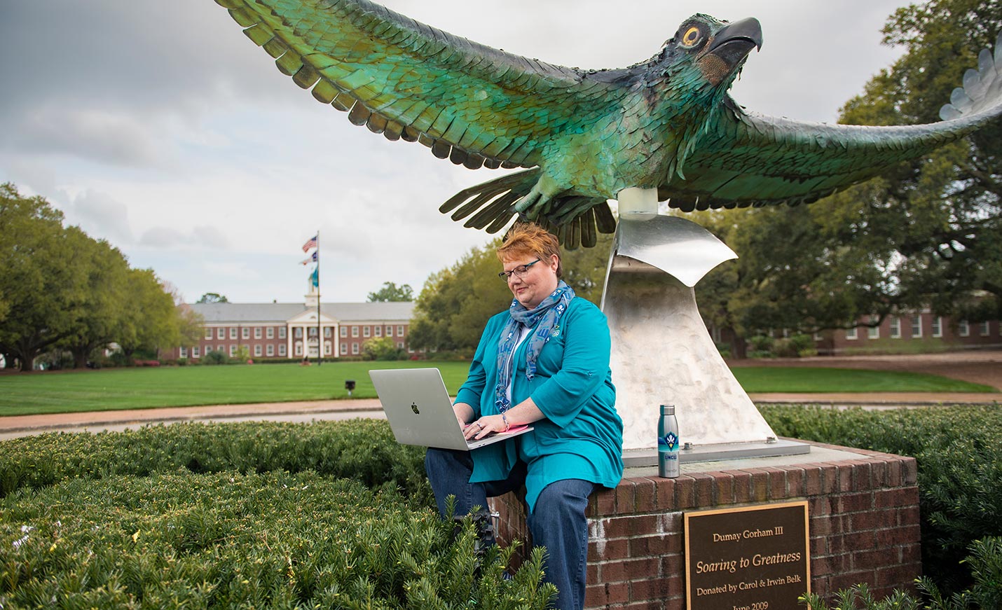 student sitting by the Seahawk statue at the front of campus