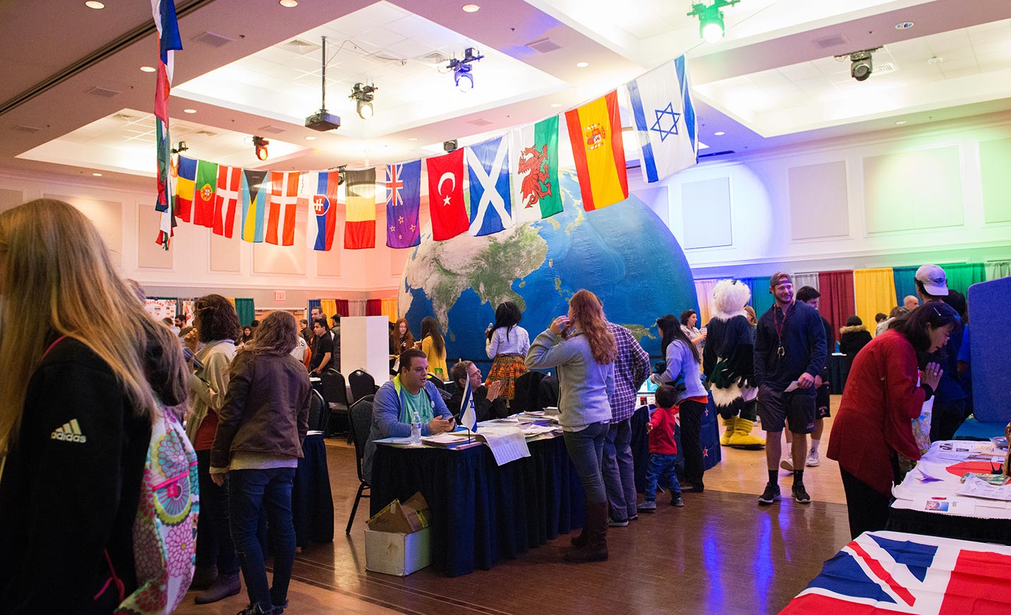 Various national flags hang overhead while visitors mill around at the Intercultural Festival