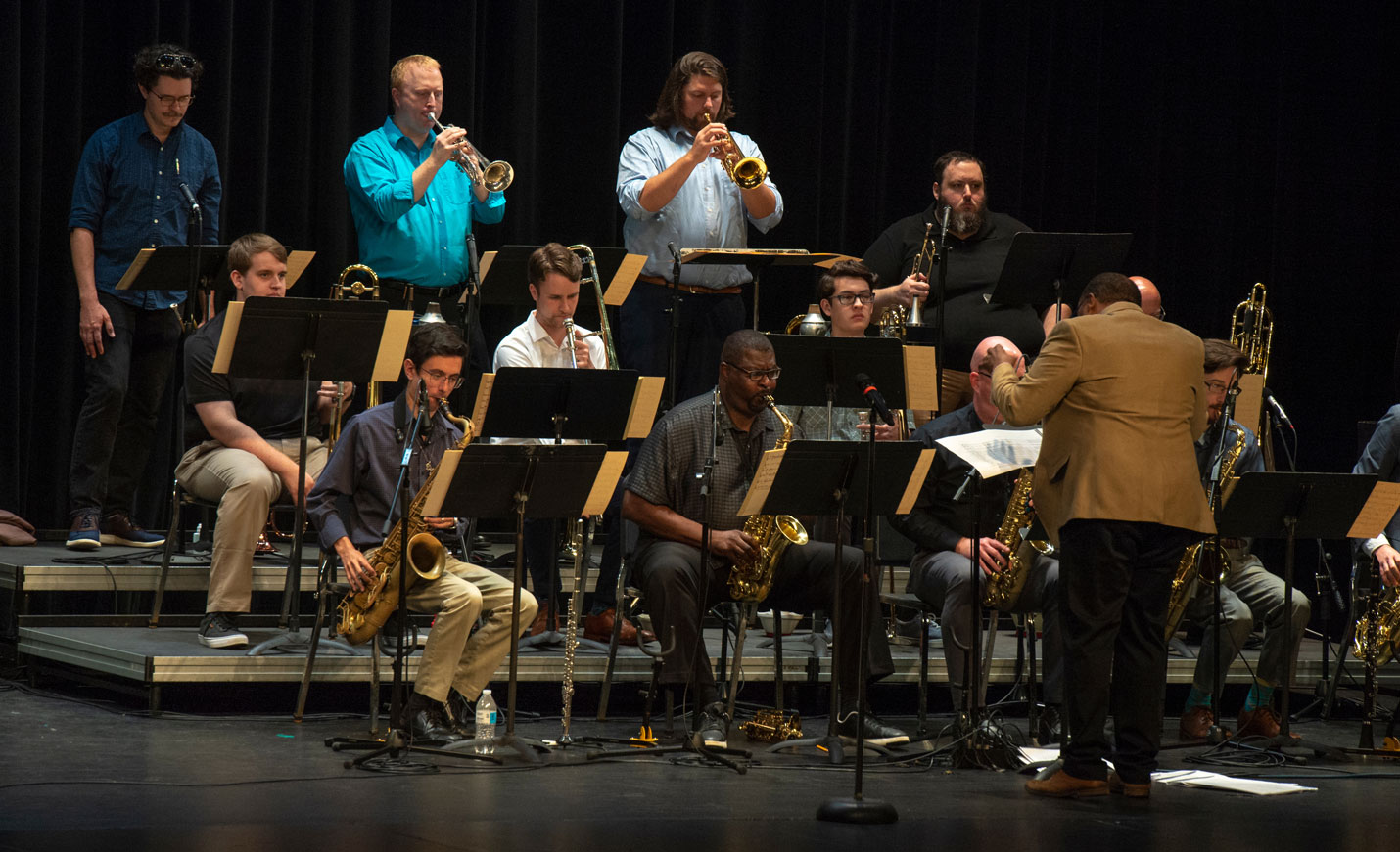 A group of musicians playing brass instruments while one man with his back to the camera conducts