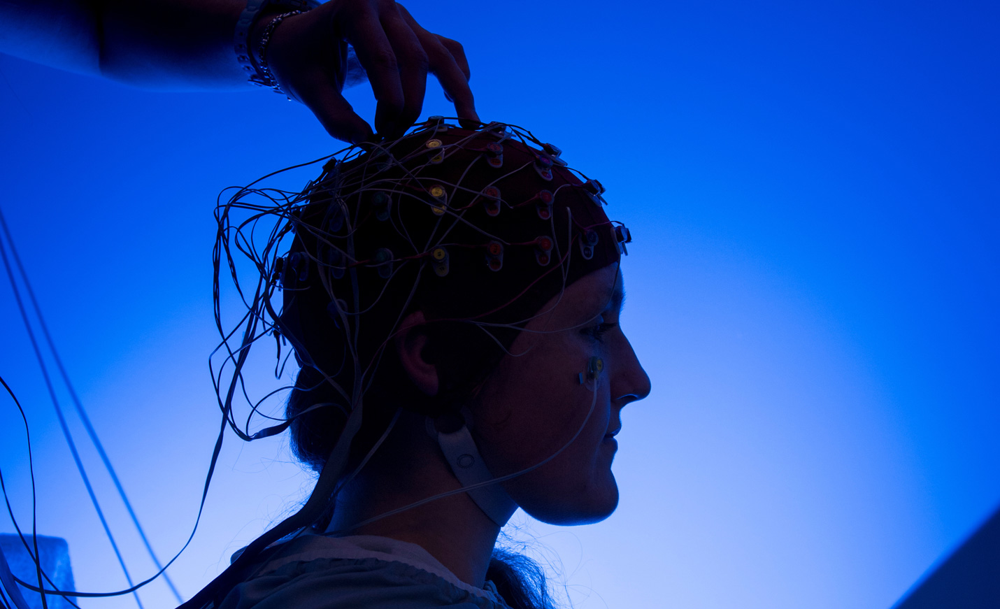 A neck-up profile photo of someone with dozens of electrodes and wires attached to their scalp