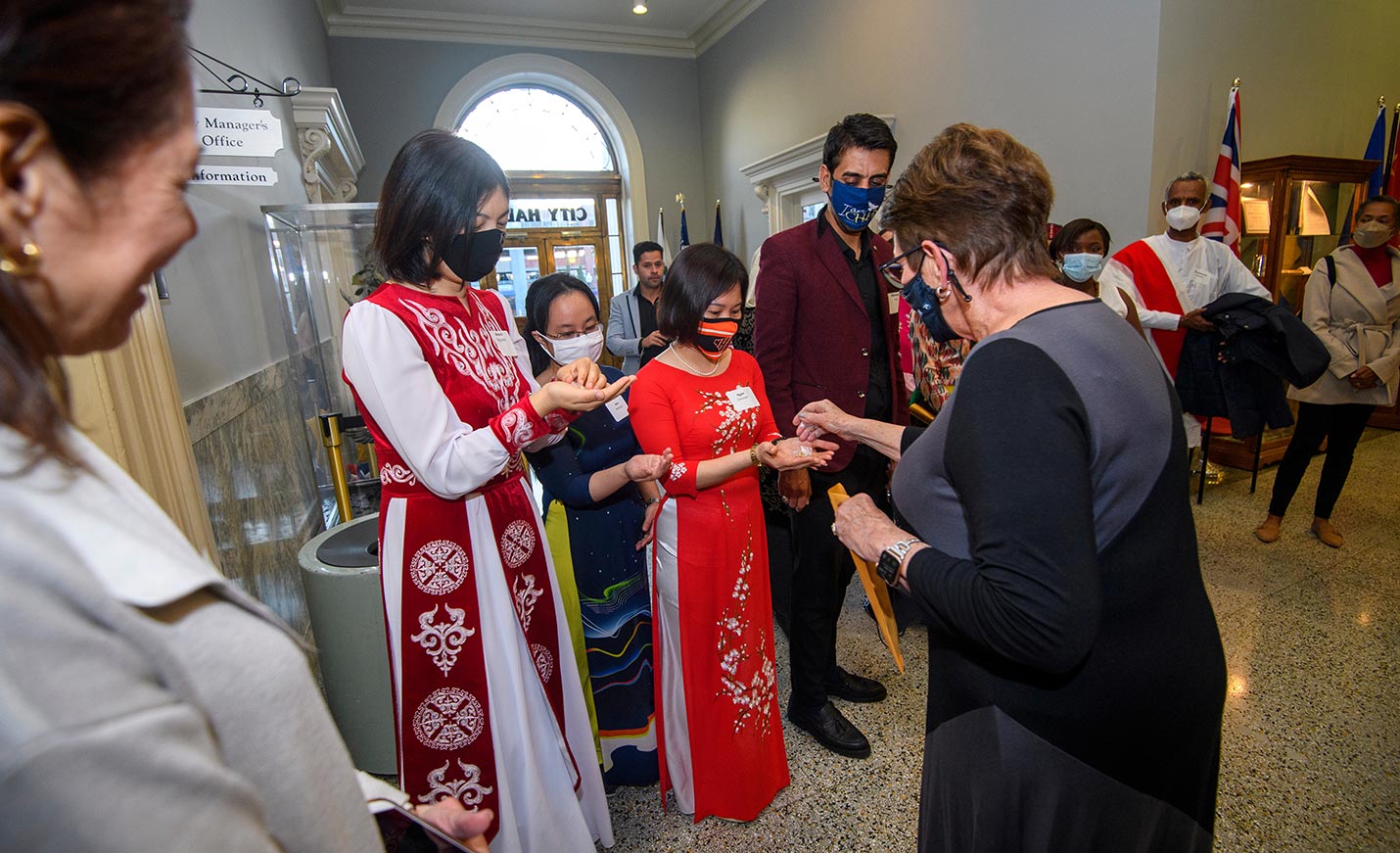 Women in ceremonial dress and masks receive gifts in the lobby of Wilmington City Hall
