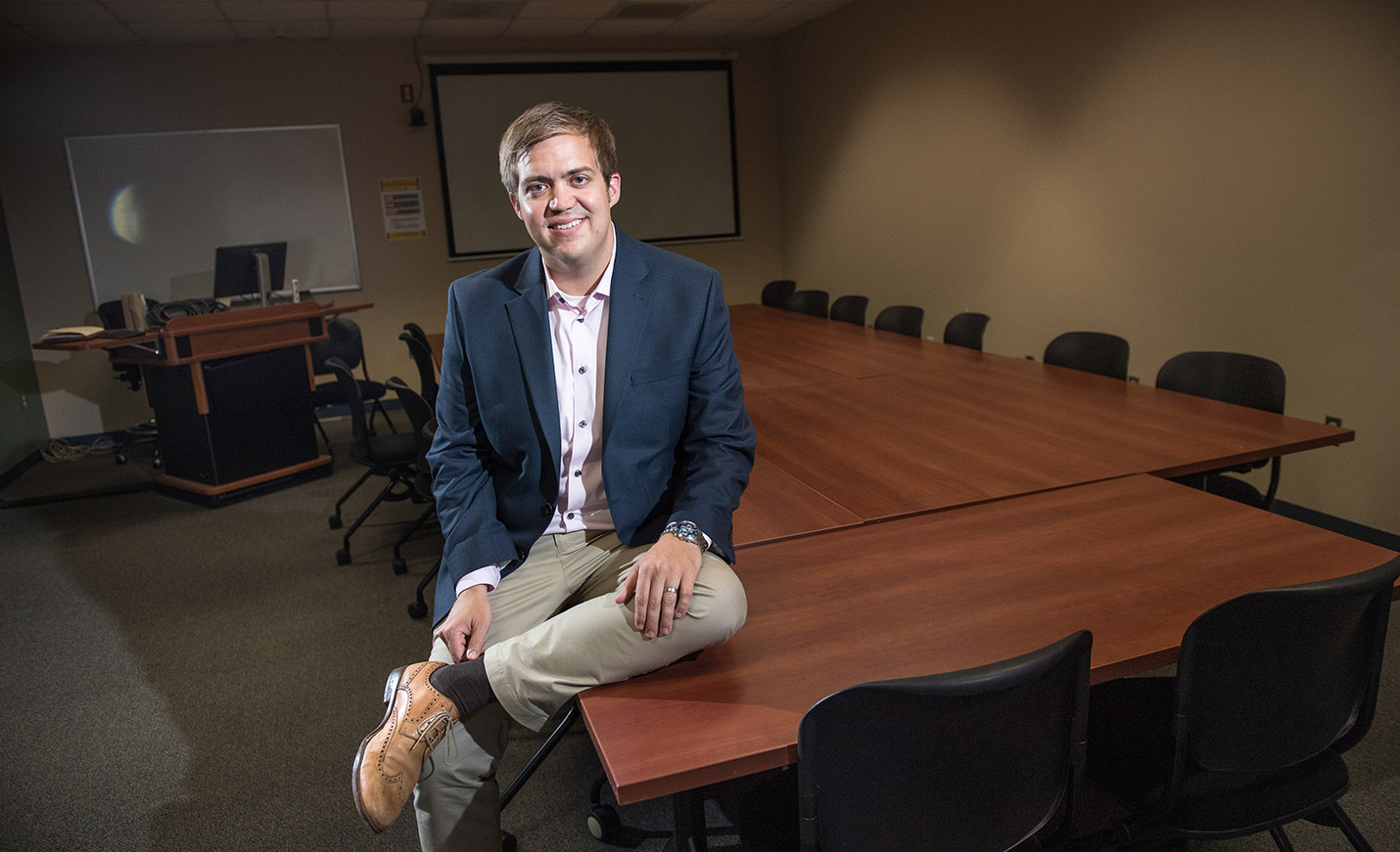 UNCW Associate Professor Aaron King sits against a table in a classroom