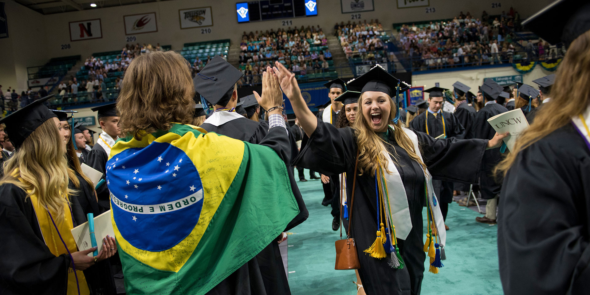 During commencement, a student wrapped in the Brazil flag gives someone a high five