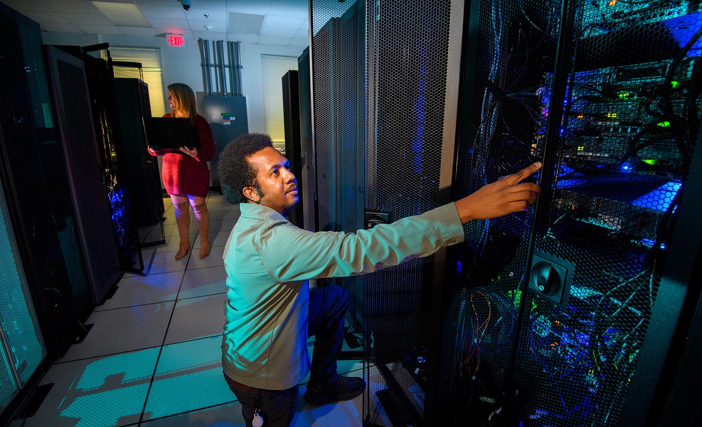 Two people work on large circuit boards in a darkened room