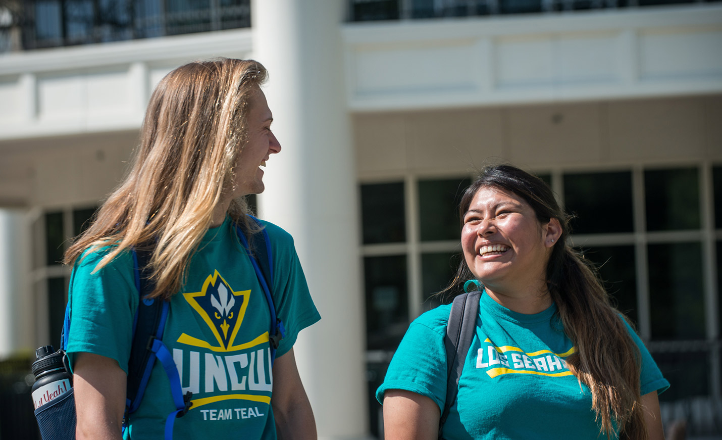 Two women in UNCW Team Teal T-shirts share a laugh