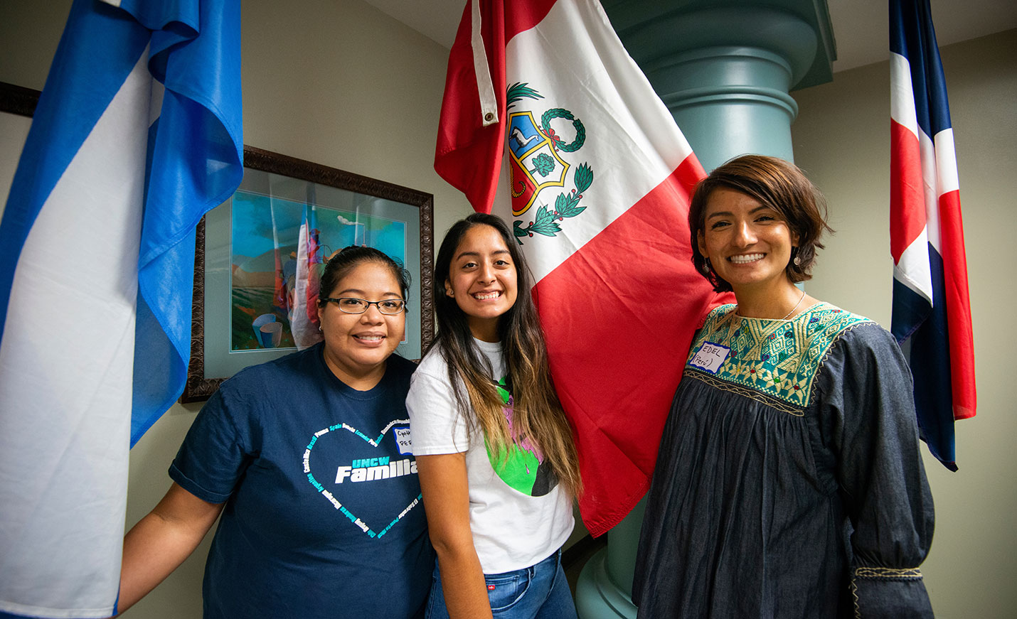 Two students and Edelmira Segovia stand in front of a flag of Peru