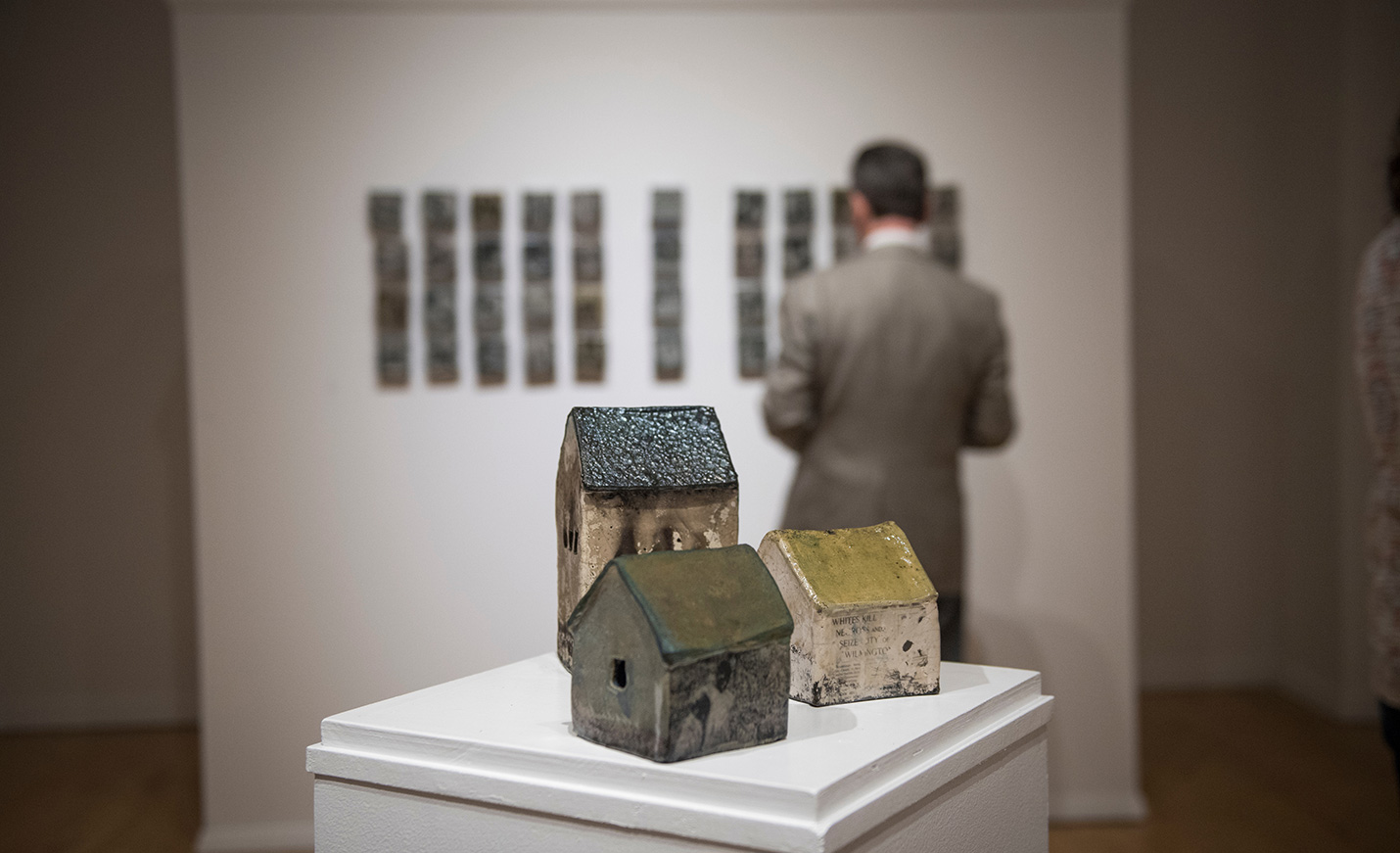 Three ceramic houses sit on a display table inside an art gallery