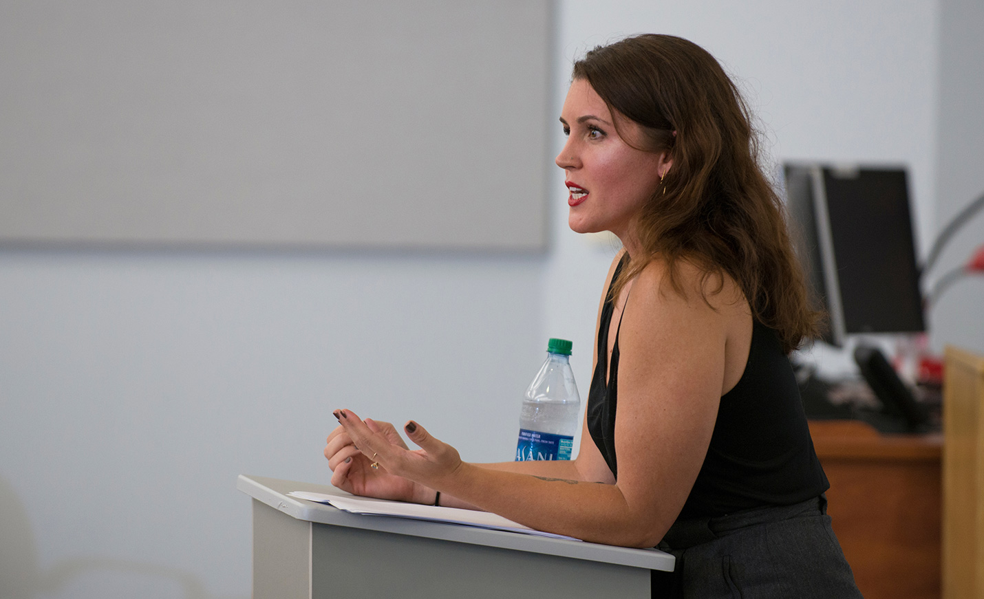 An instructor stands at a lectern with a bottle of water next to her