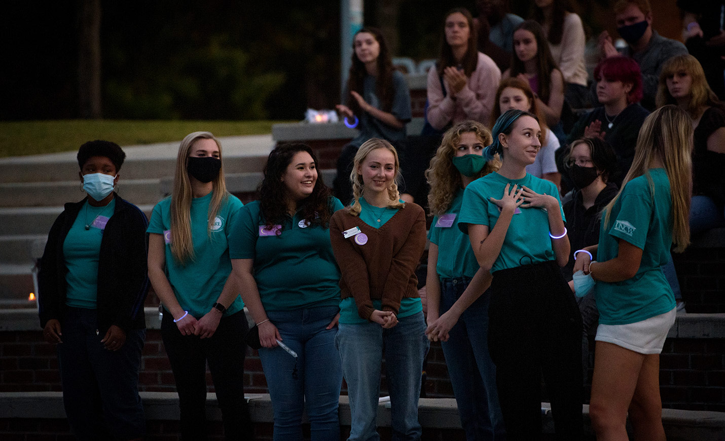 A group of women in UNCW attire, some masked, listen while another woman shares her thoughts