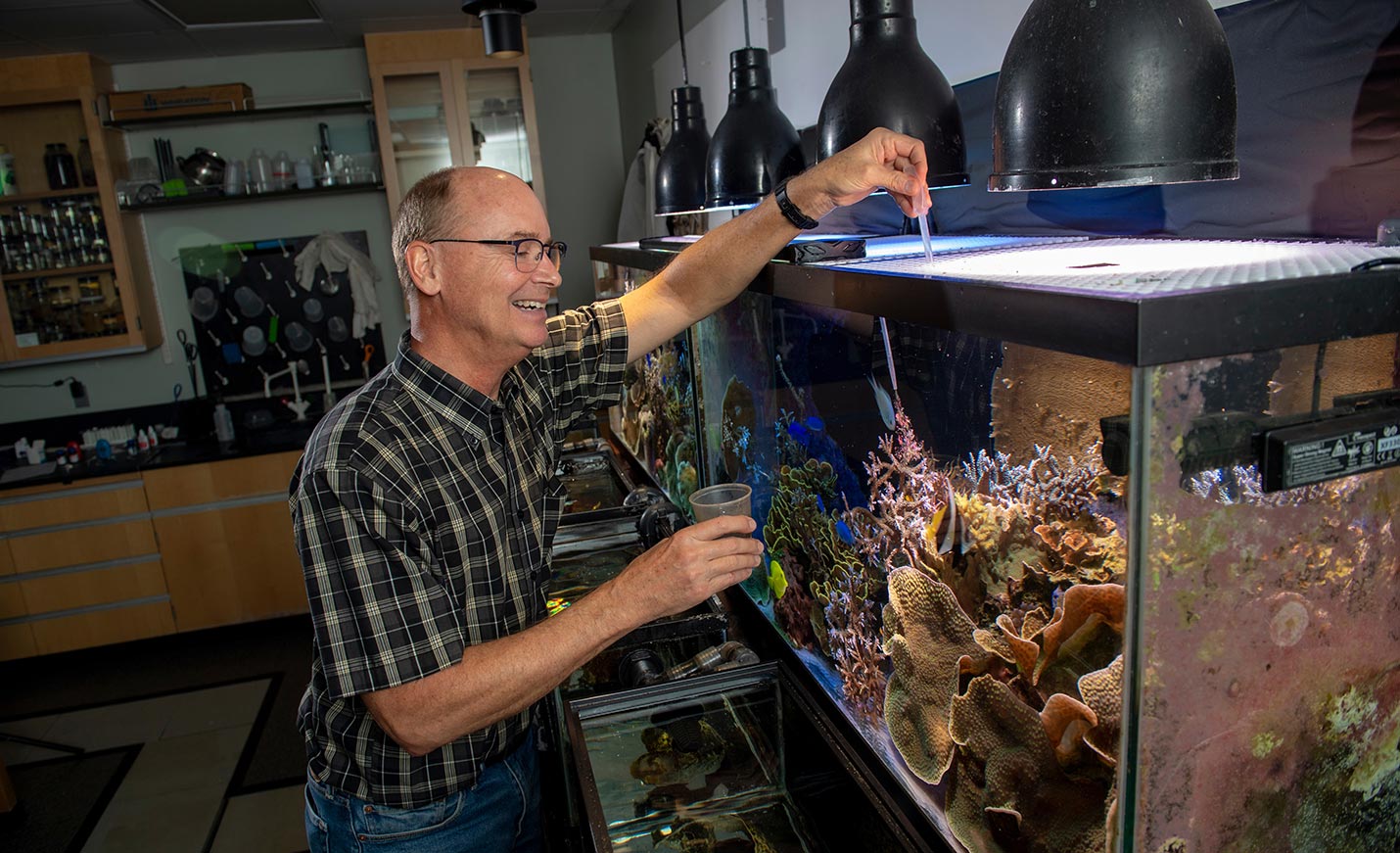 A professor takes a water sample from a fish tank in a marine science lab