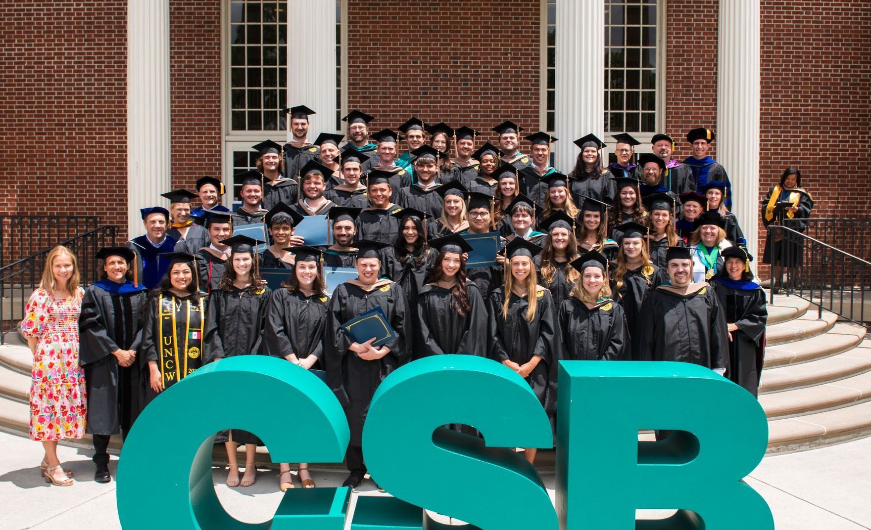 CSB MS Accountancy graduates posing behind large teal CSB letters on the steps.