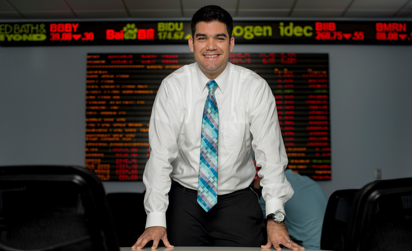 Associate Professor of Economics and Finance Daniel Soques stands in front of the stocks ticker inside Congdon Hall