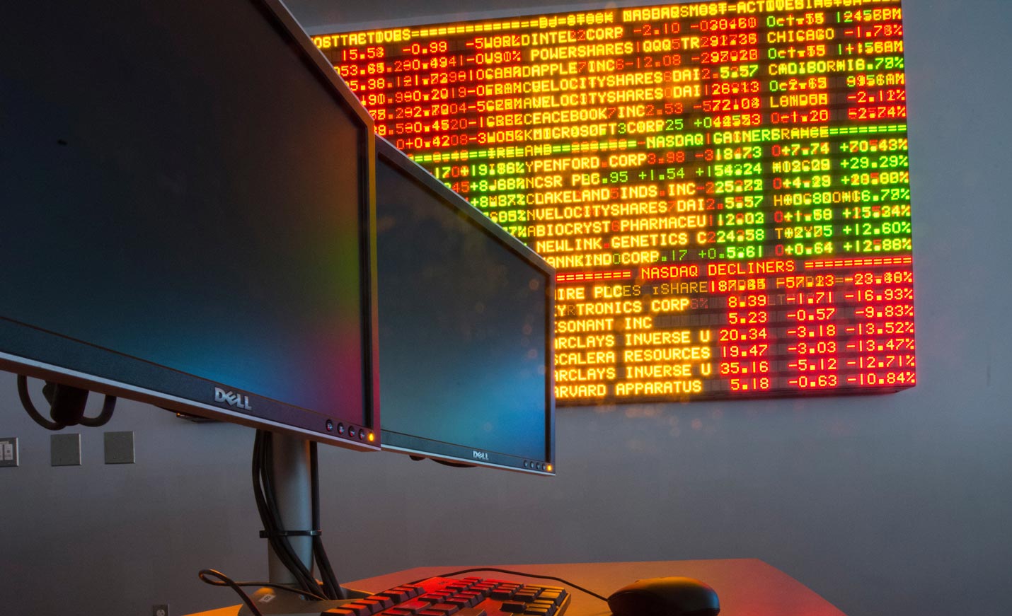 Computer monitors in the foreground with the stocks ticker in Congdon Hall in the background