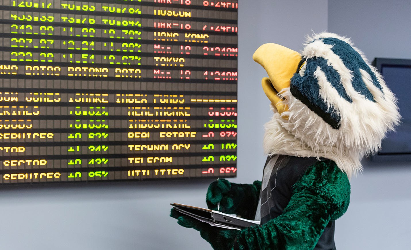 Sammy C. Hawk stands taking notes while looking at a stock ticker board