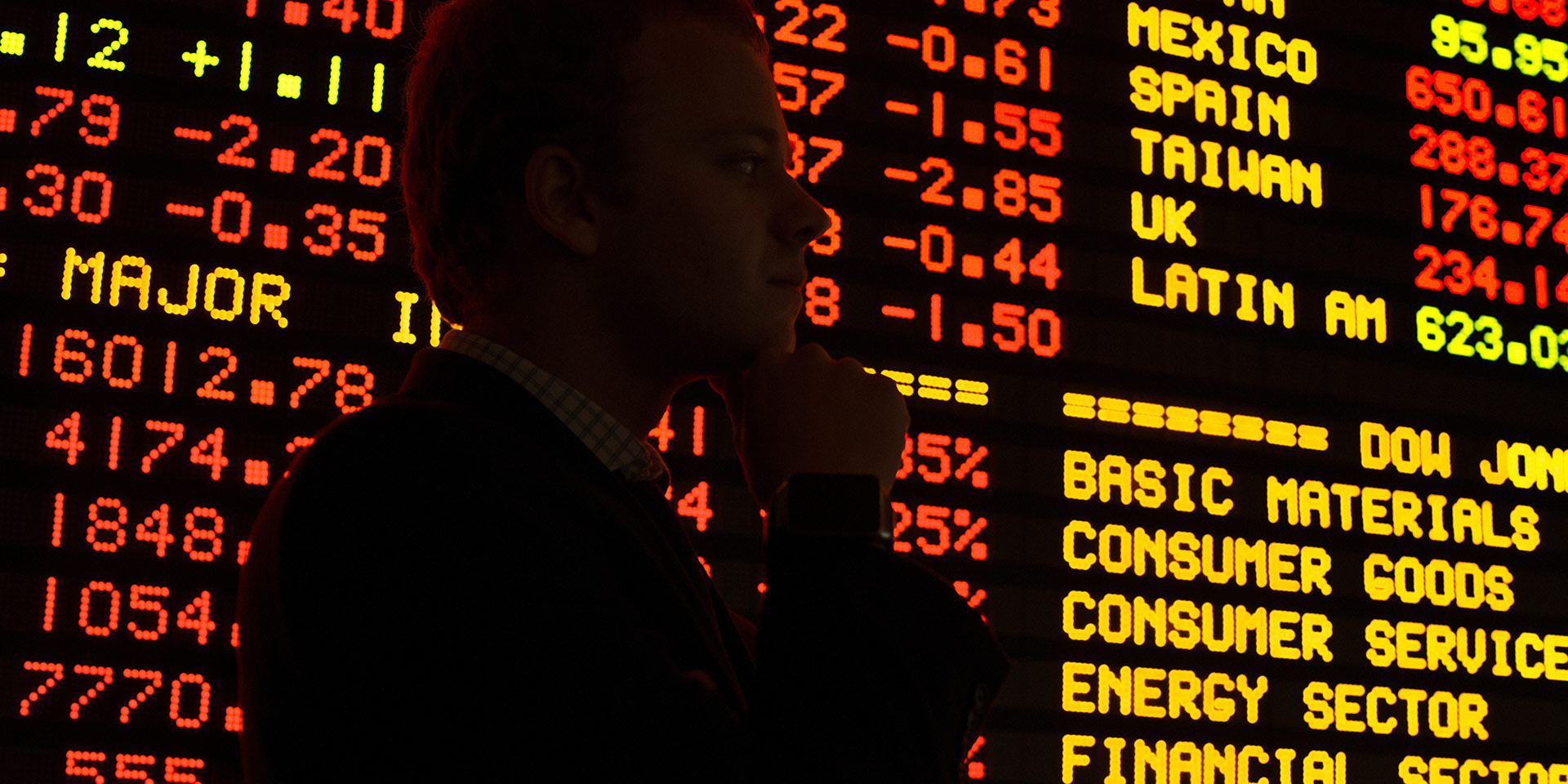 A person stands in front of a large stock ticker board