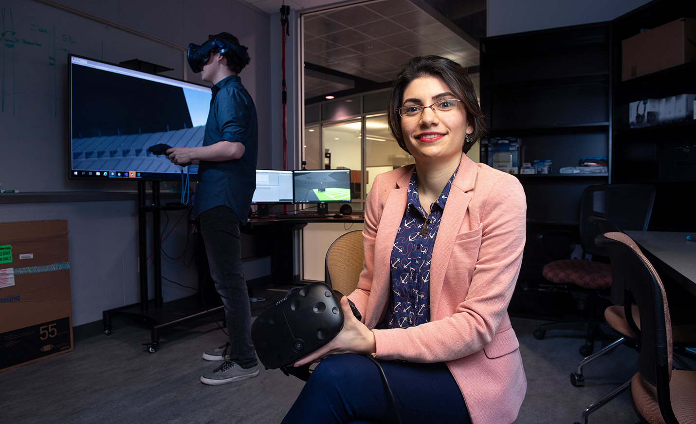 A student in virtual reality headgear stands in the background; a faculty member faces the camera in the foreground. Caption on the photo reads FURTHER YOUR EXPERIENCE IN COMPUTER SCIENCE