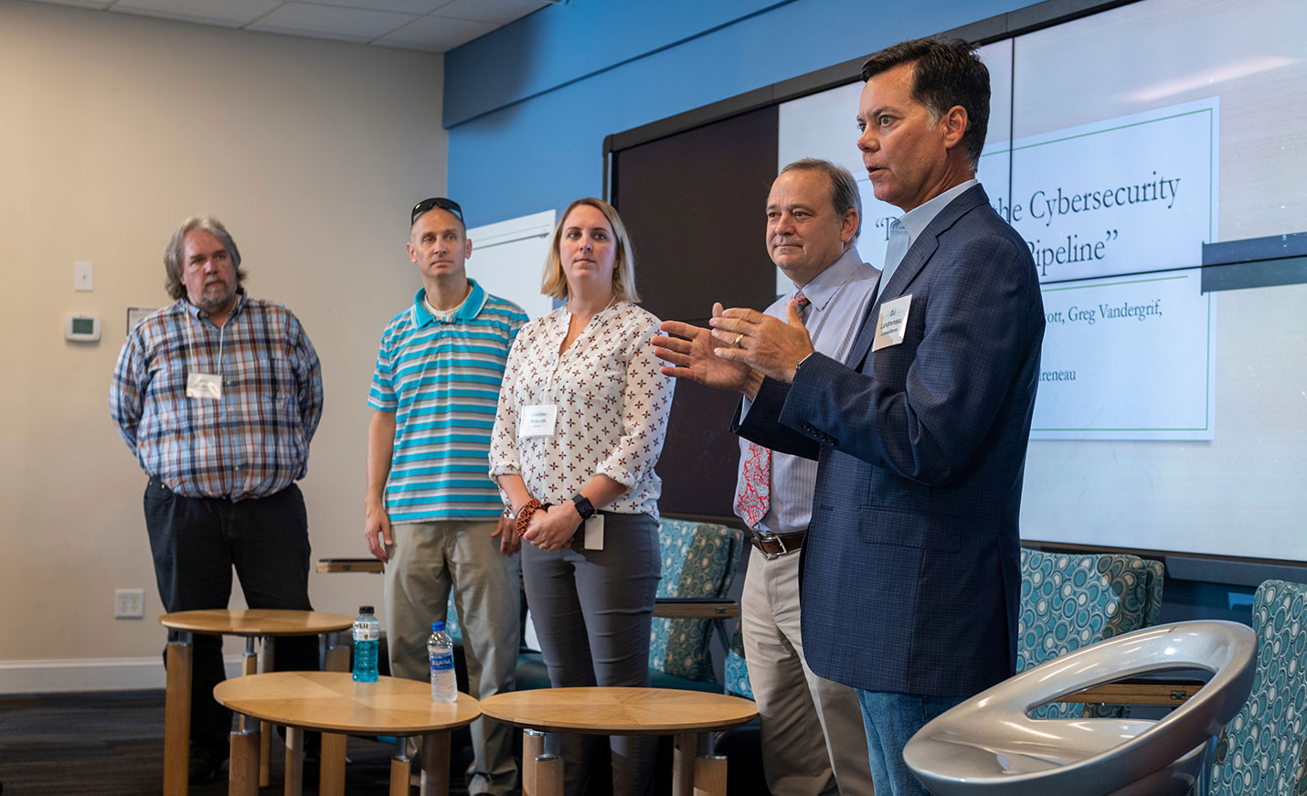A speaker standing with a group of other presenters talks at a cybersecurity event