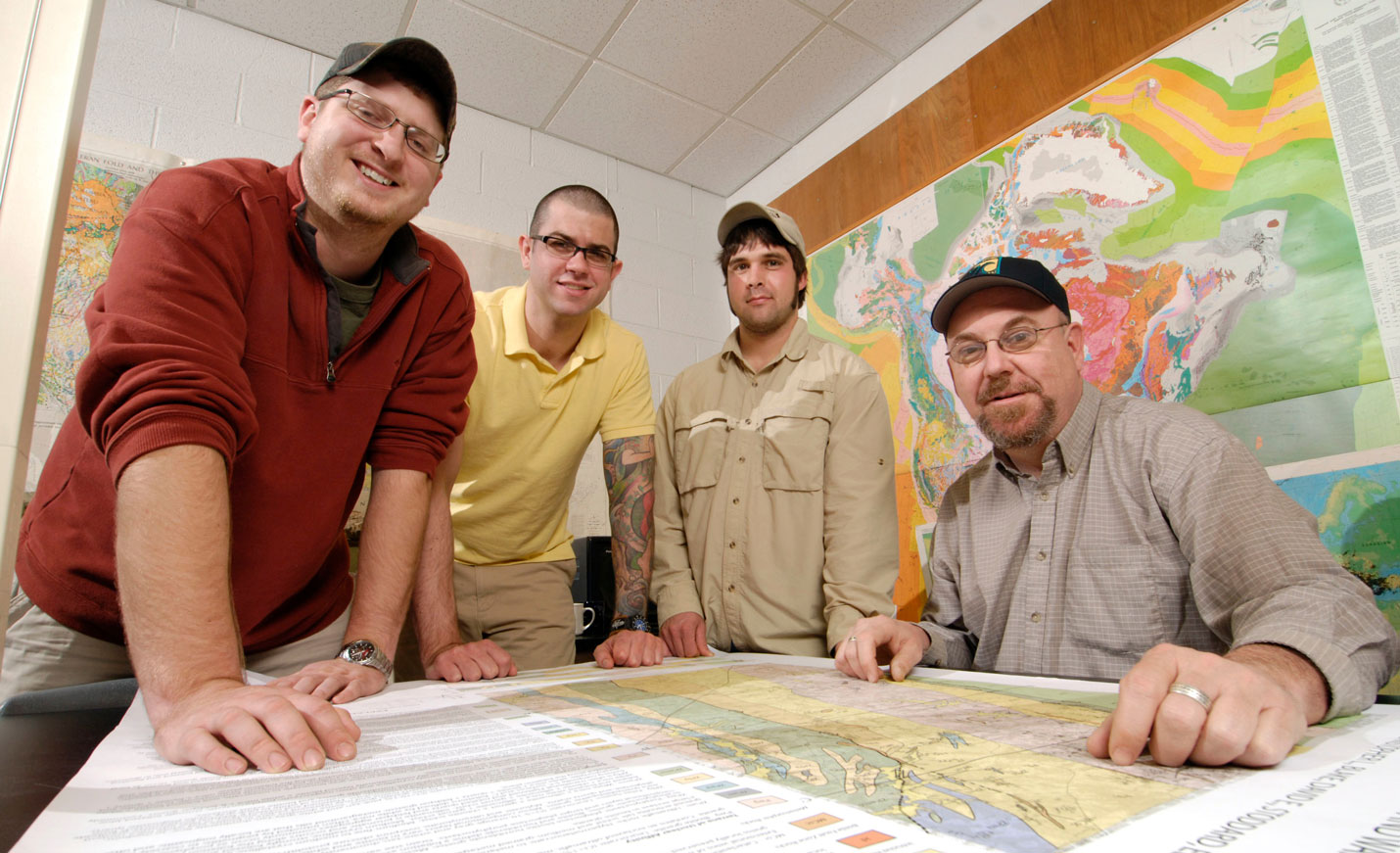 A group of geology professors smiles for the camera while looking over a map