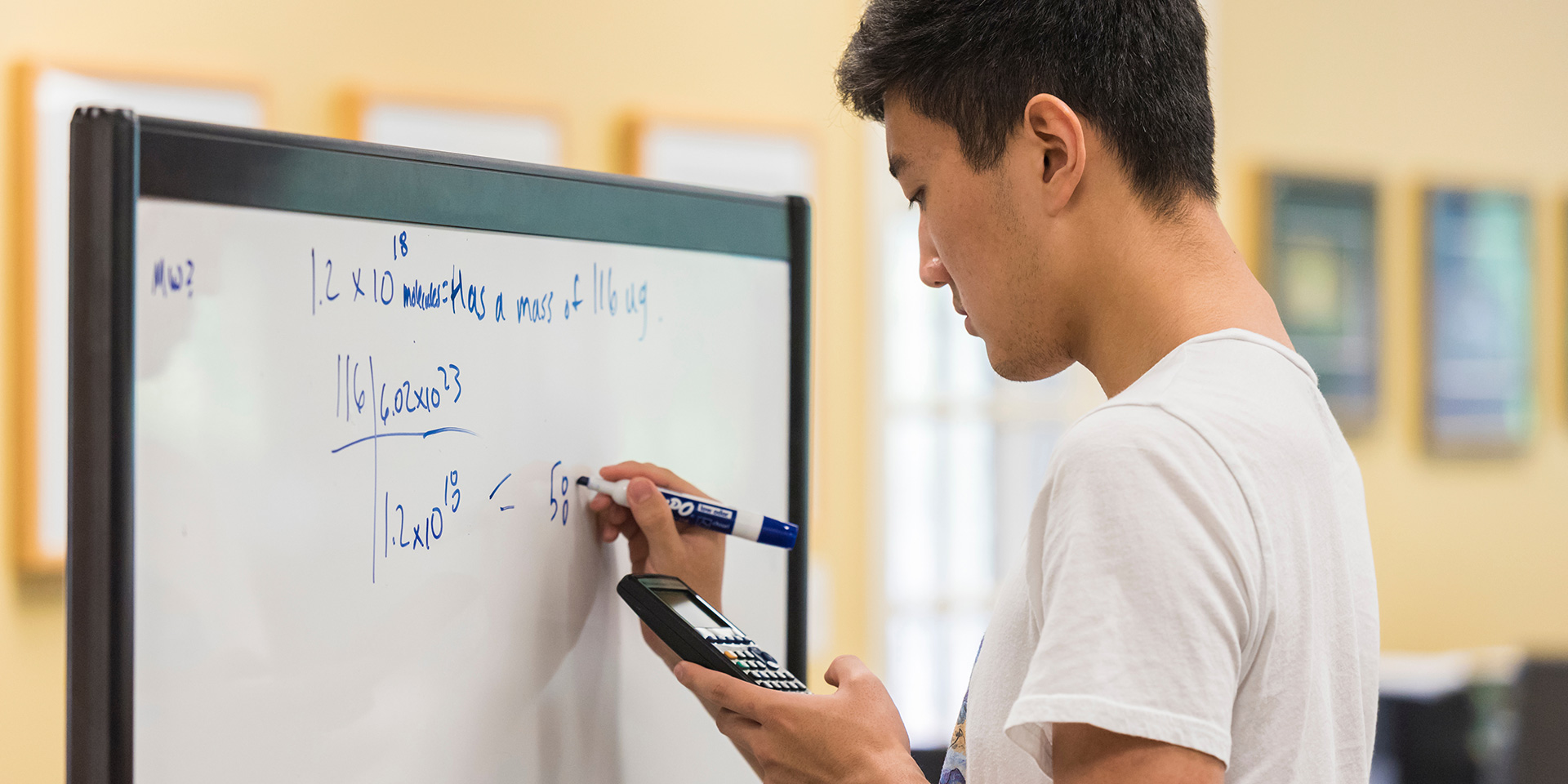A student using a whiteboard to solve a math equation