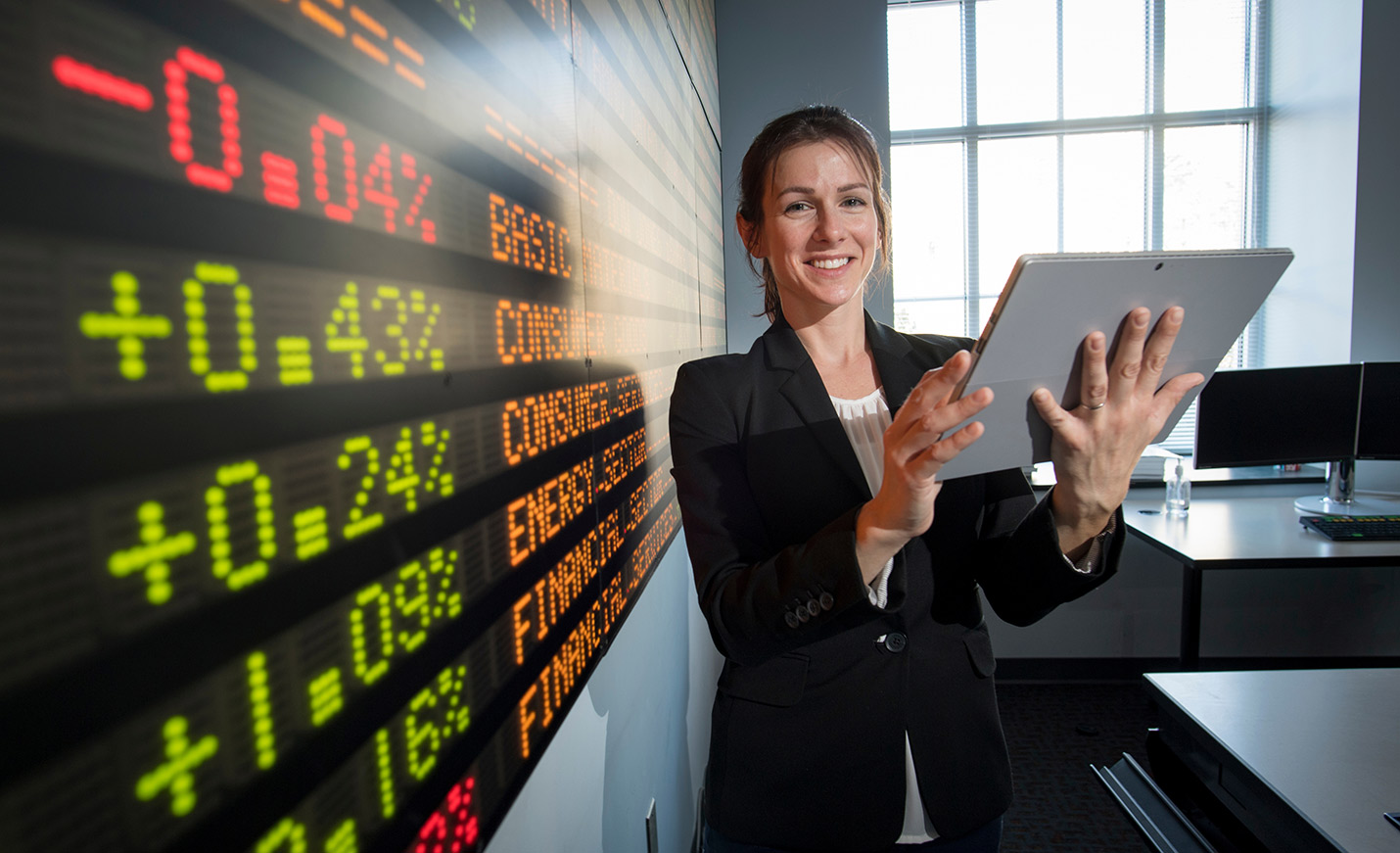 A person holding a tablet next to a stock ticker board 