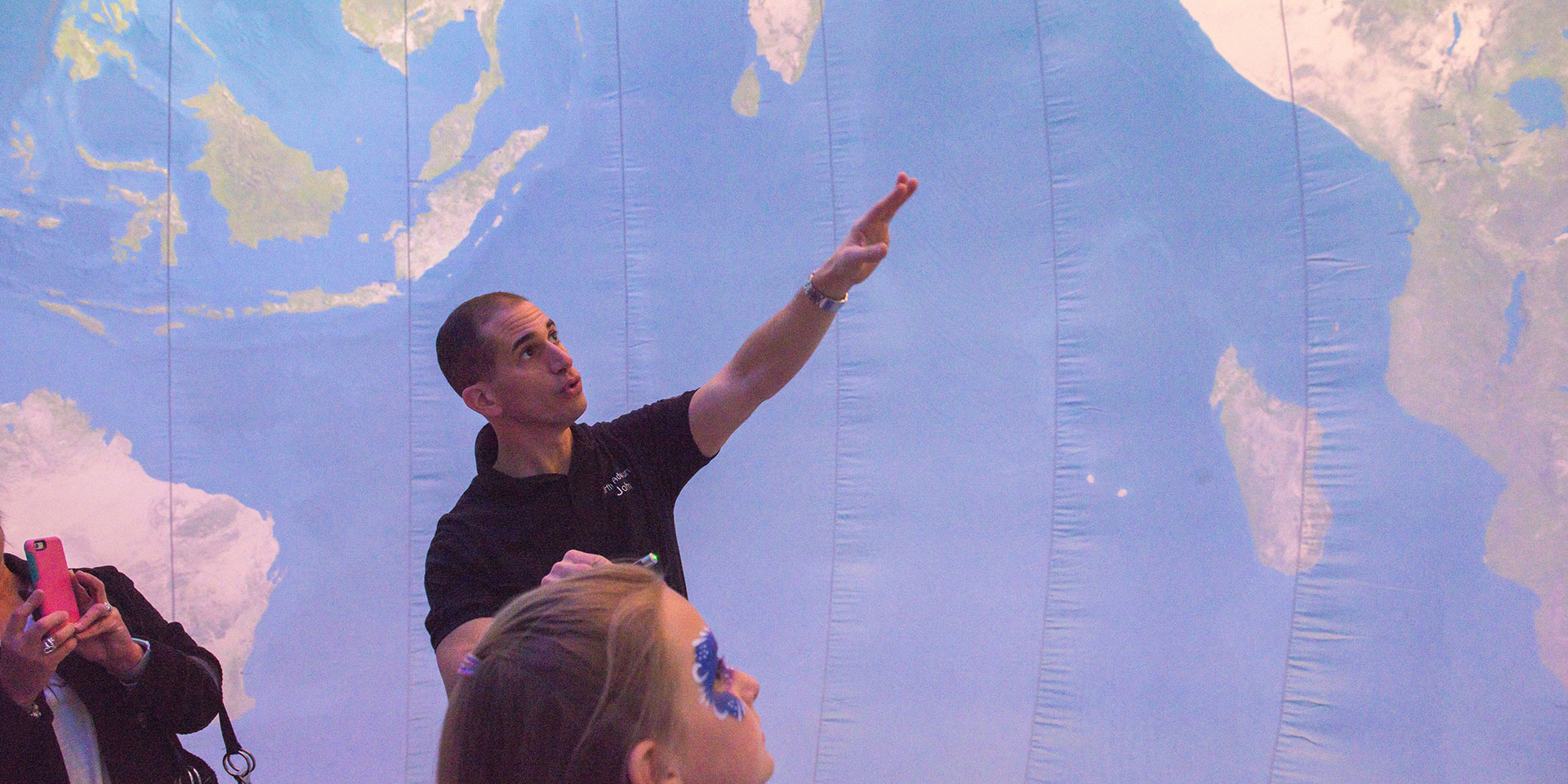 A professor standing inside an inflatable globe points to a part of the map for a group of students