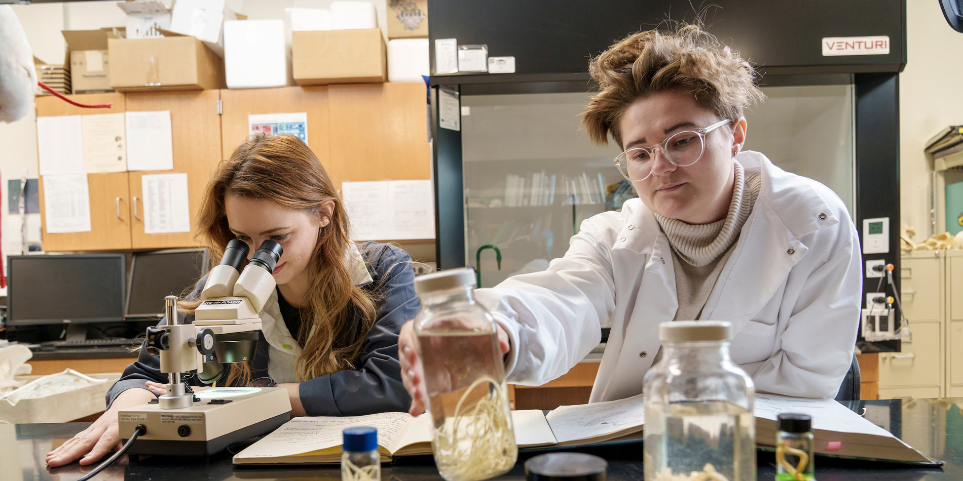 Students in a lab with jars and a microscope