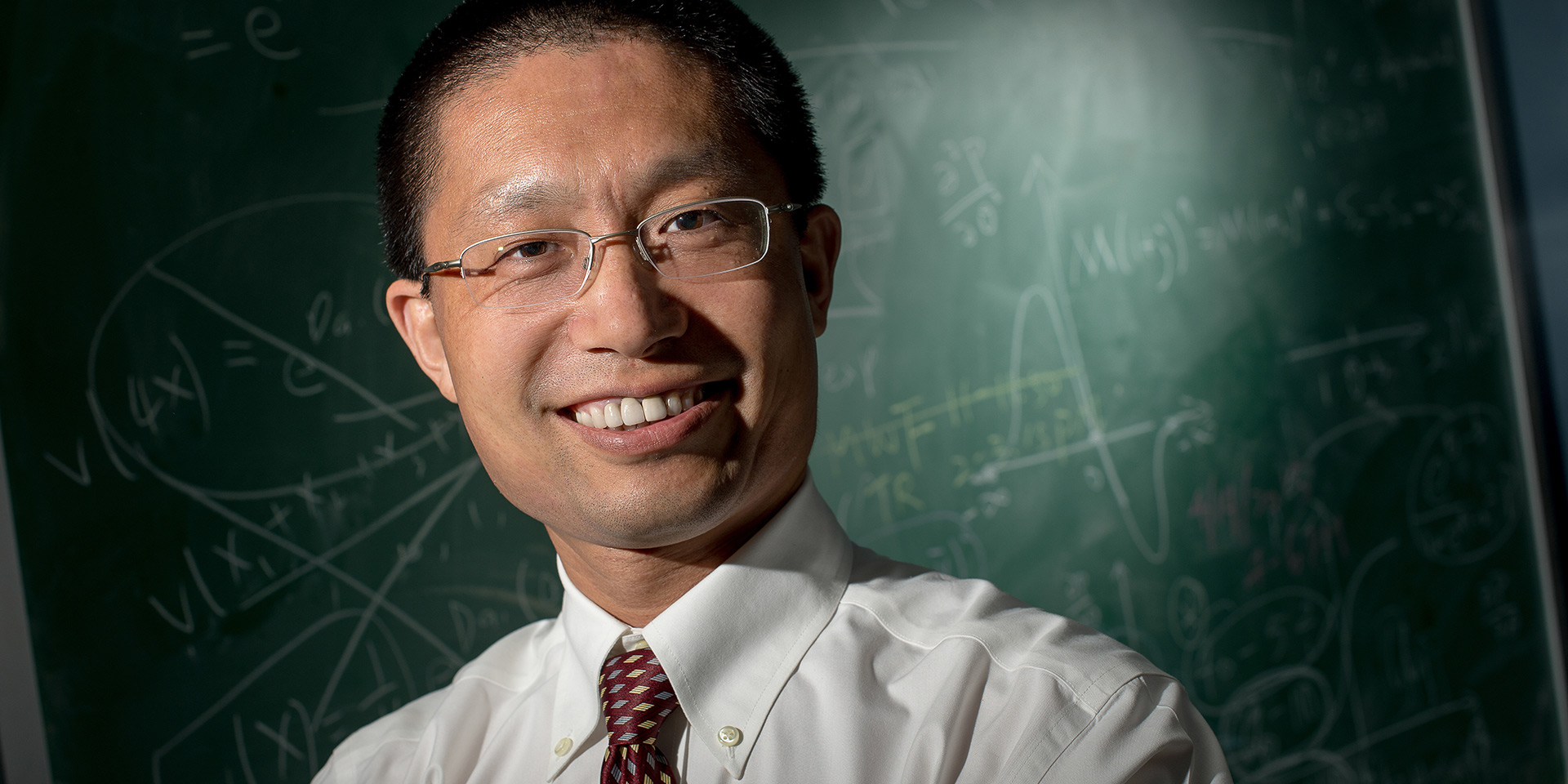 A professor standing in front of a chalkboard filled with math equations
