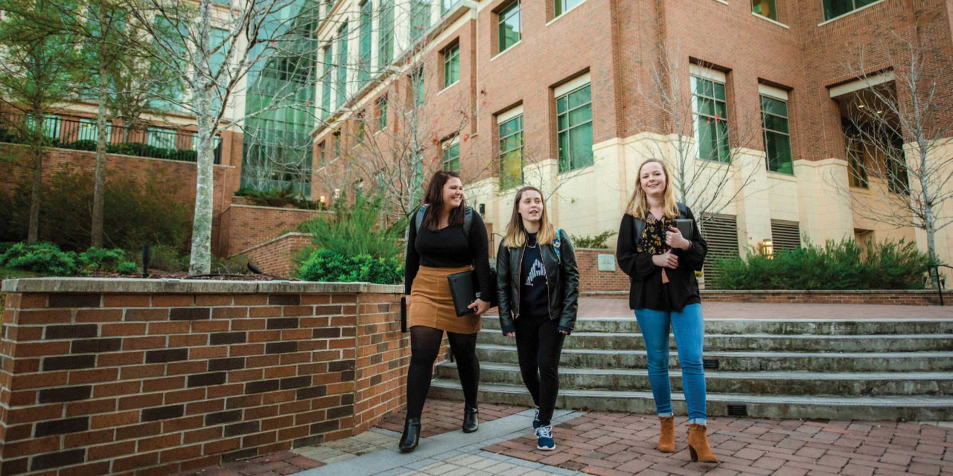 Three Watson students holding a portfolio walking down a staircase outside of a building