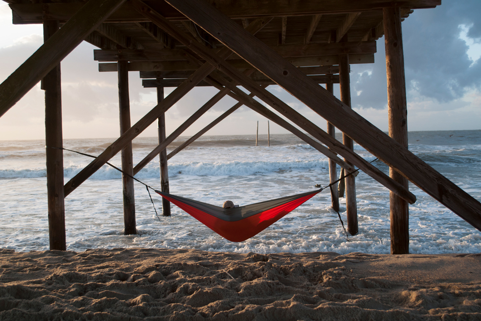 Student relaxing in a hammock under a pier at the beach