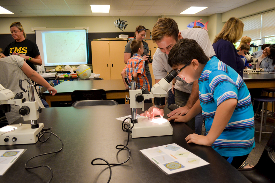 Watson student helping a middle grades student look through a microscope
