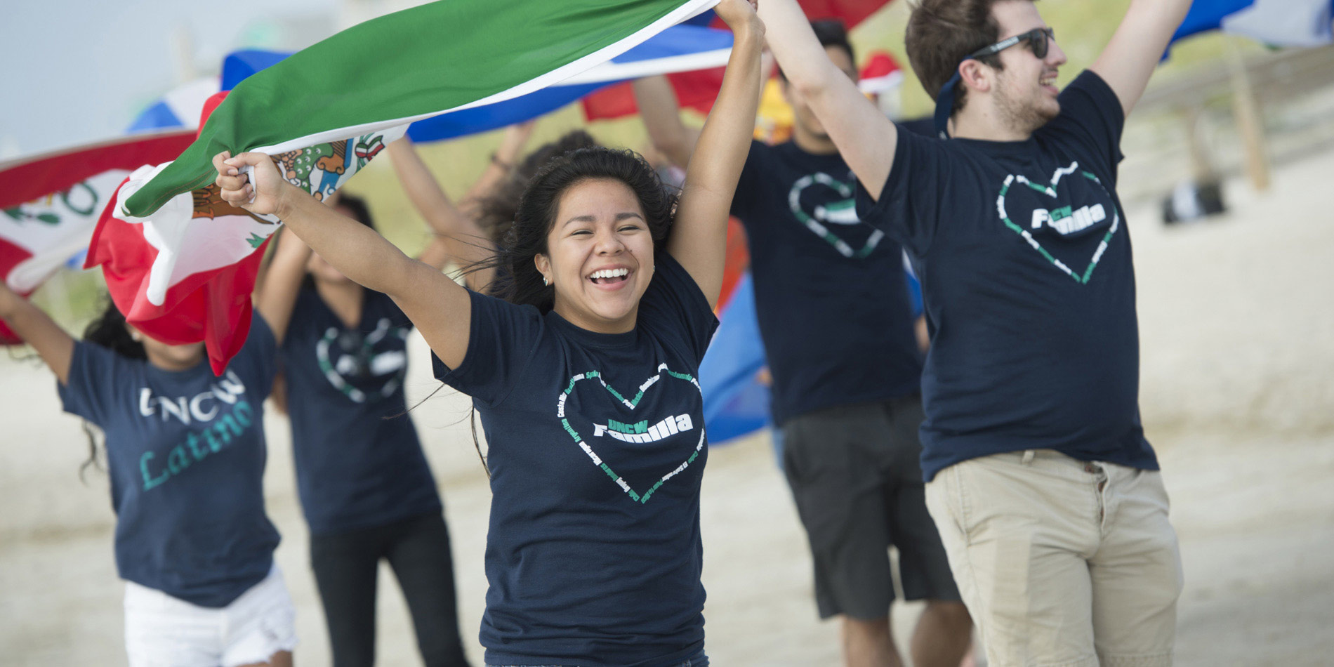 Watson students holding a flag together above their heads running along the beach