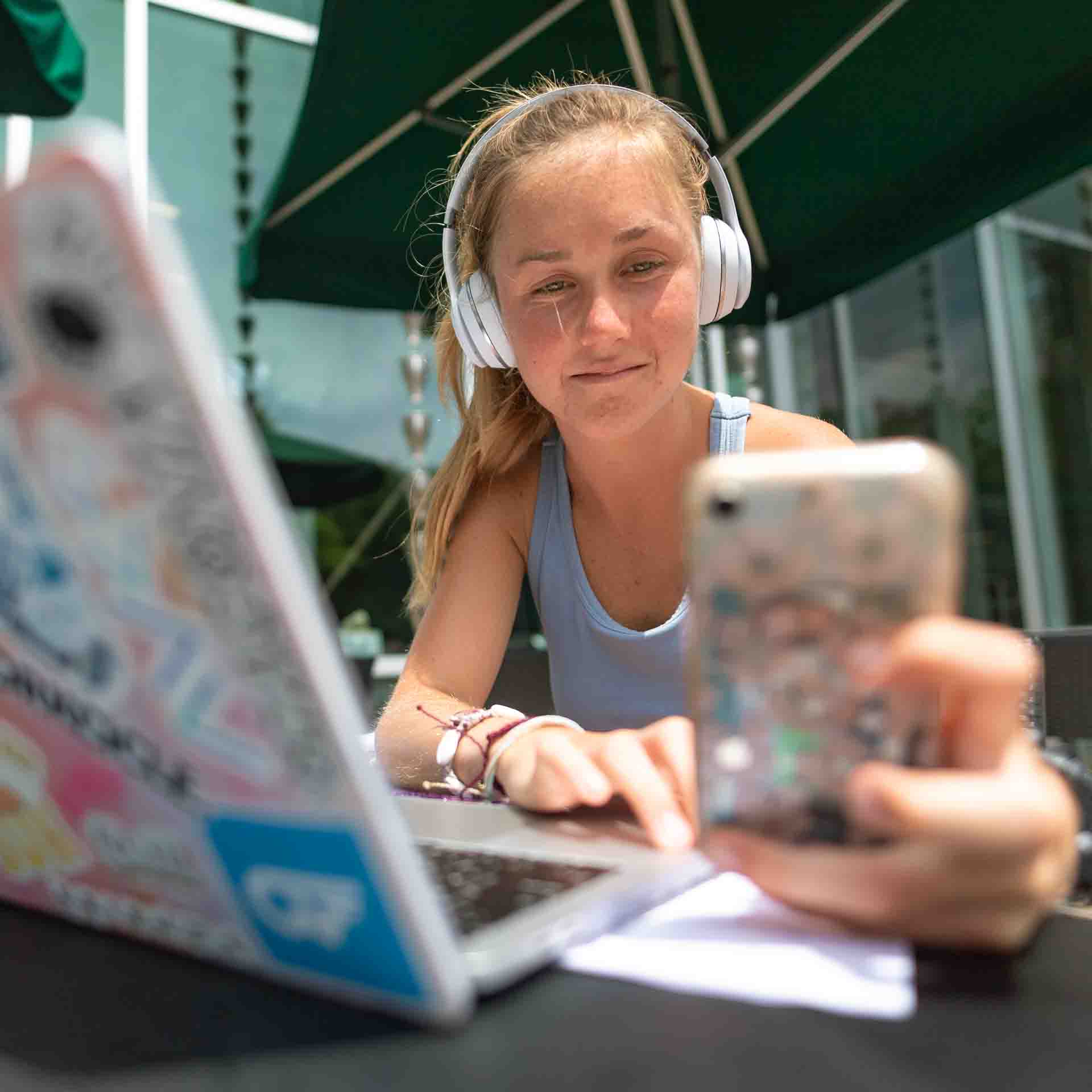 Girl using phone, headphones and laptop.