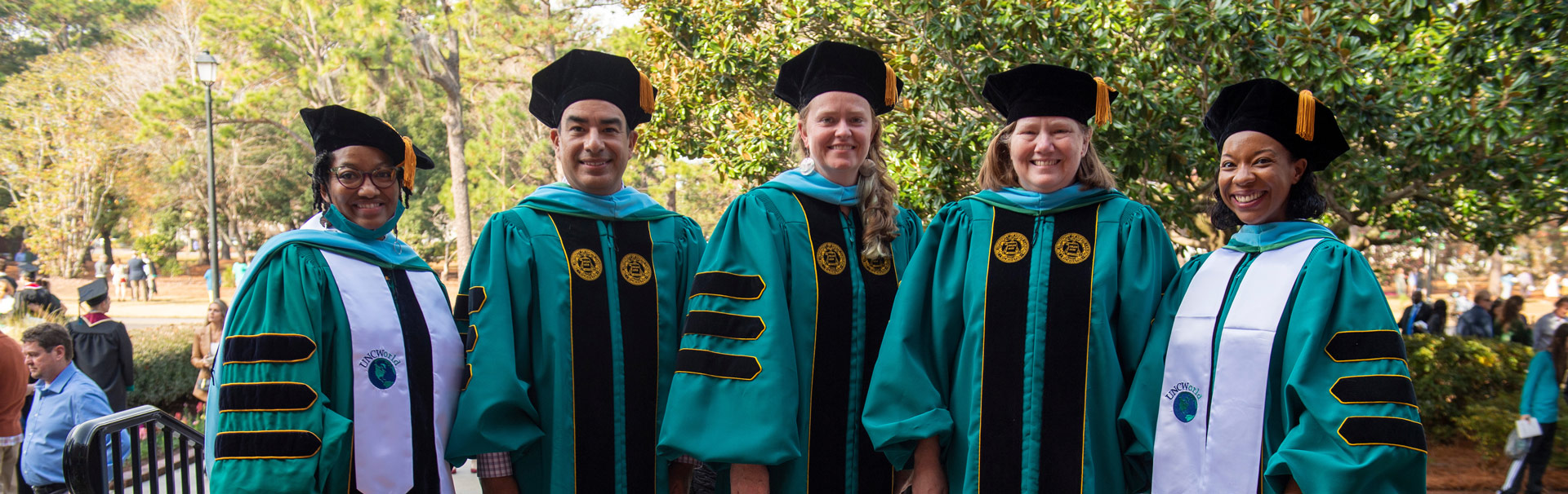 Five professors wearing graduation gowns standing outside Trask Coliseum