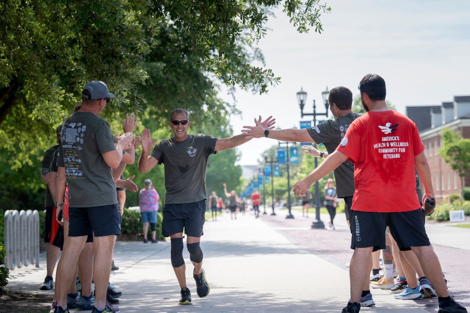 Runners slap their hands together on a sidewalk with trees and a building in the background.