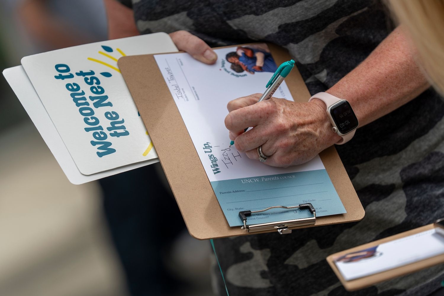 Person writing on a clipboard beside a sign reading Welcome to the Nest.