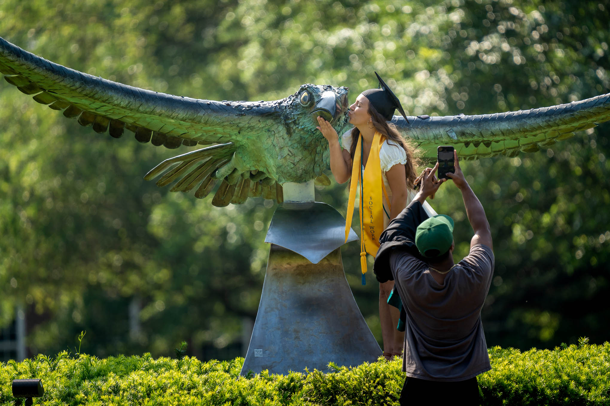 uncw graduate kisses seahawk statue with grad cap on