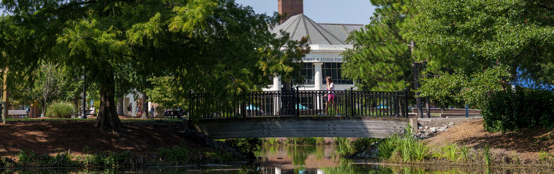 Students walking across bridge over the center campus pond