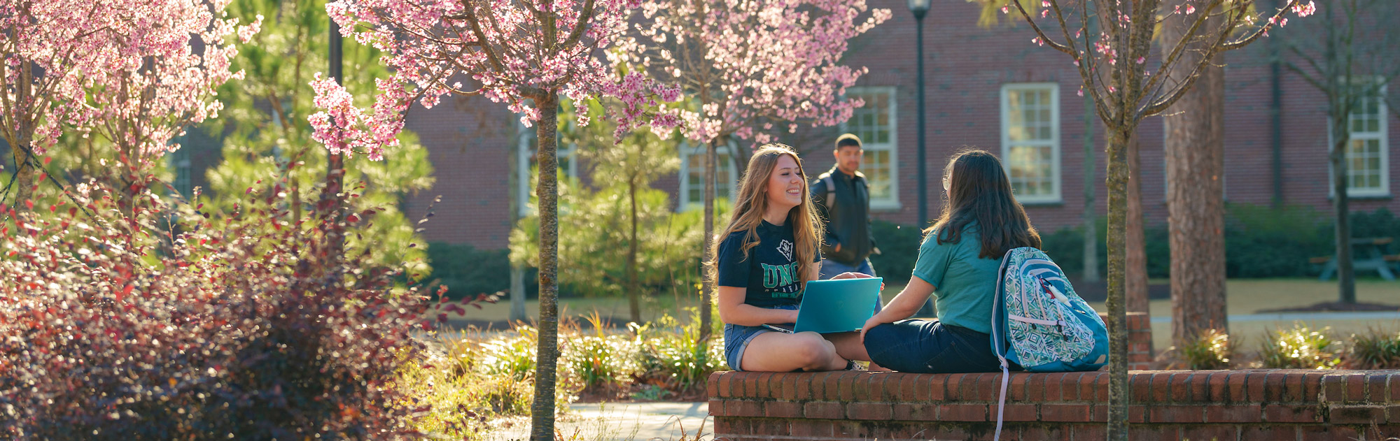 Two students sitting outside during the spring time with a teal laptop.
