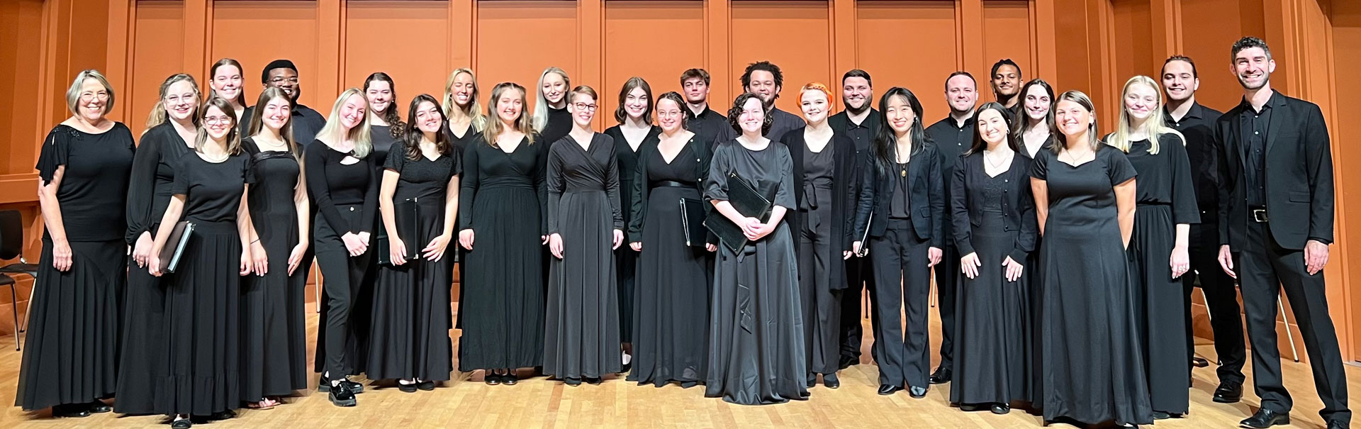 Chorus ensemble wearing all black, posing together for a photo for a performance.