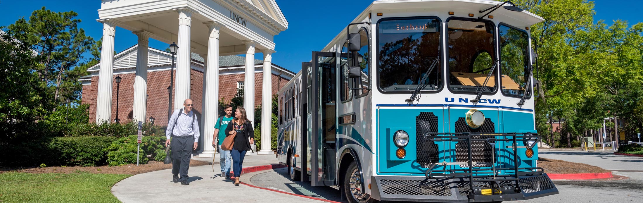 students boarding trolley in front of the UNCW columns