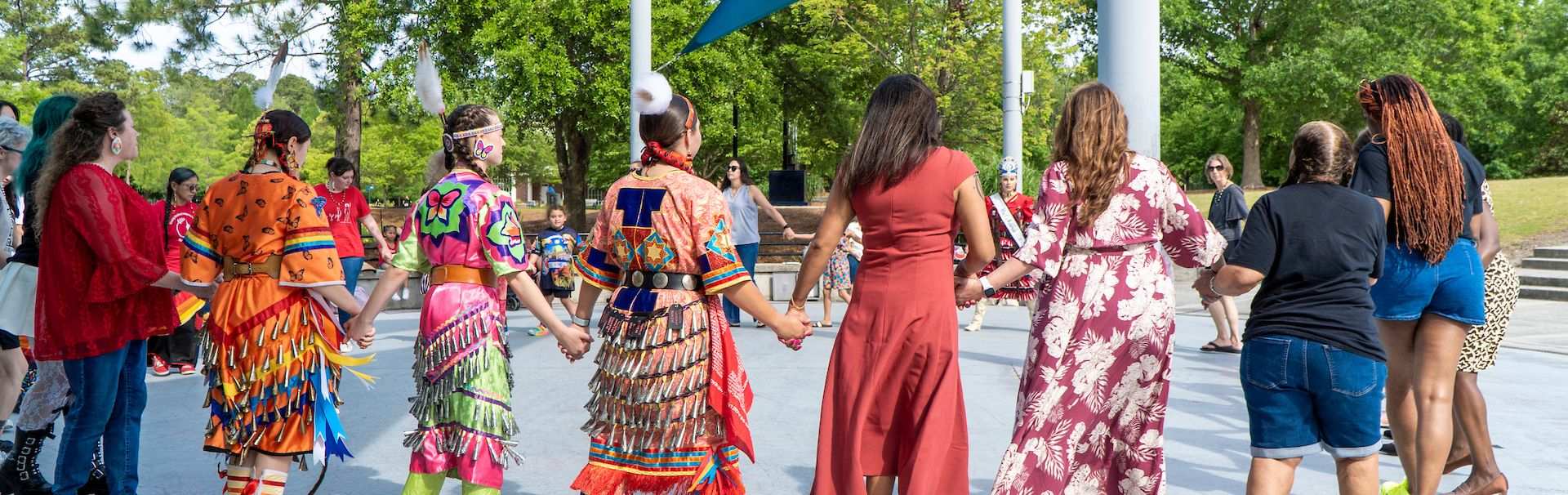 People in Indigenous garb walk hand-in-hand with others on campus