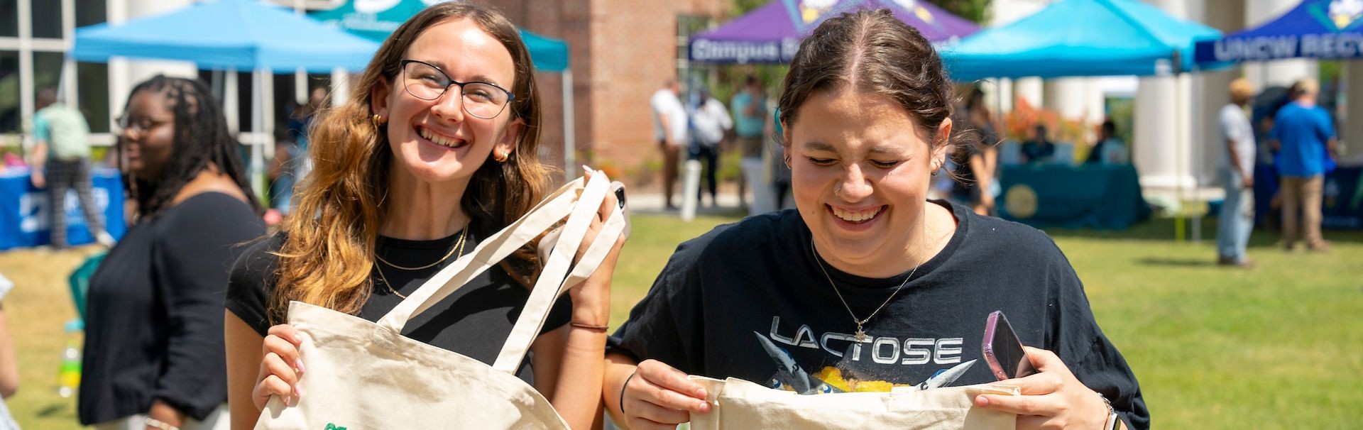 2 students holding go green tote bags