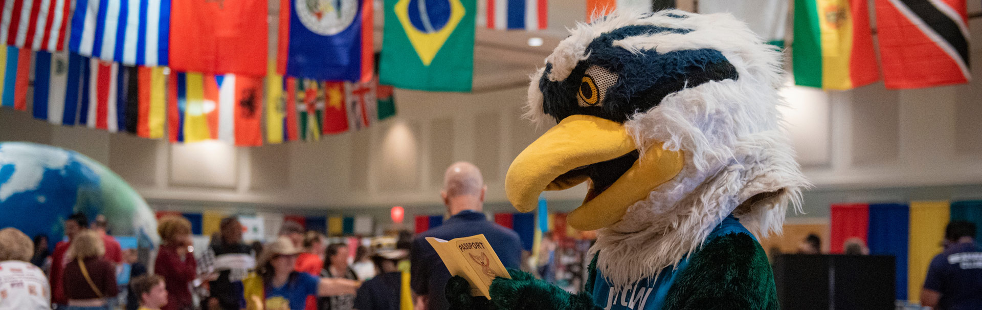 sammy seahawk holding a passport in front of flags