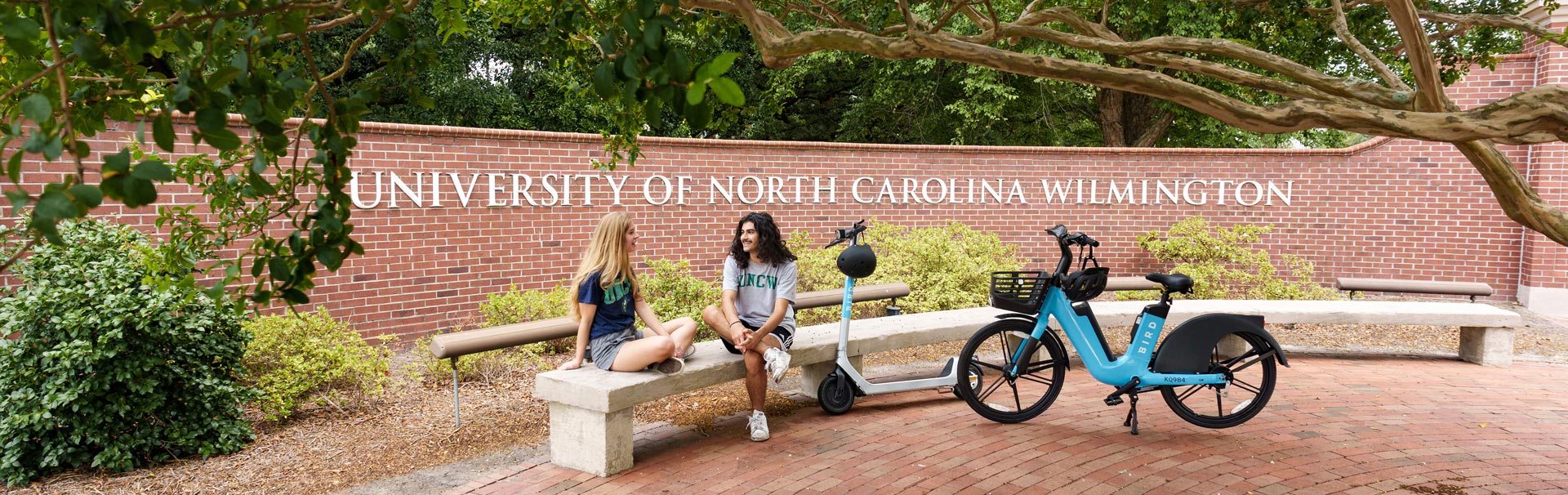 students with e-bike and scooter in front of the university entrance sign