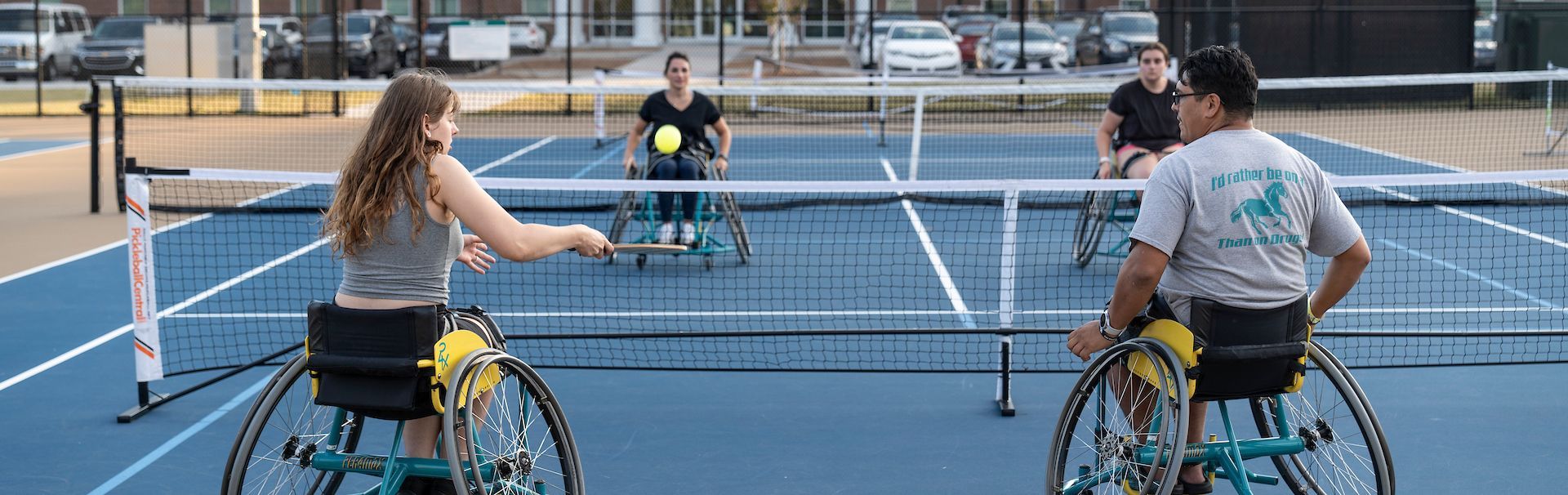 Students in wheelchairs playing pickleball at the outdoor tennis court