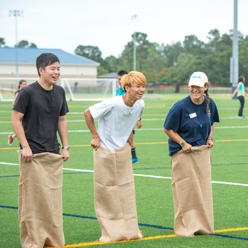 Three students holding potato sacks as they race on a field
