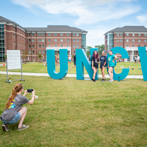 Students posing in front of the giant UNCW sign in a field