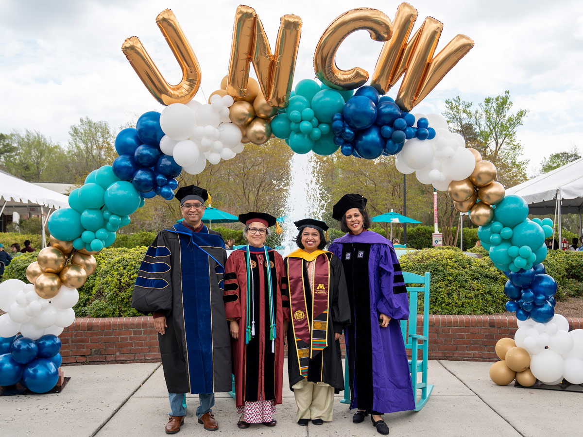 Four Faculty members pose for photo under UNCW balloons
