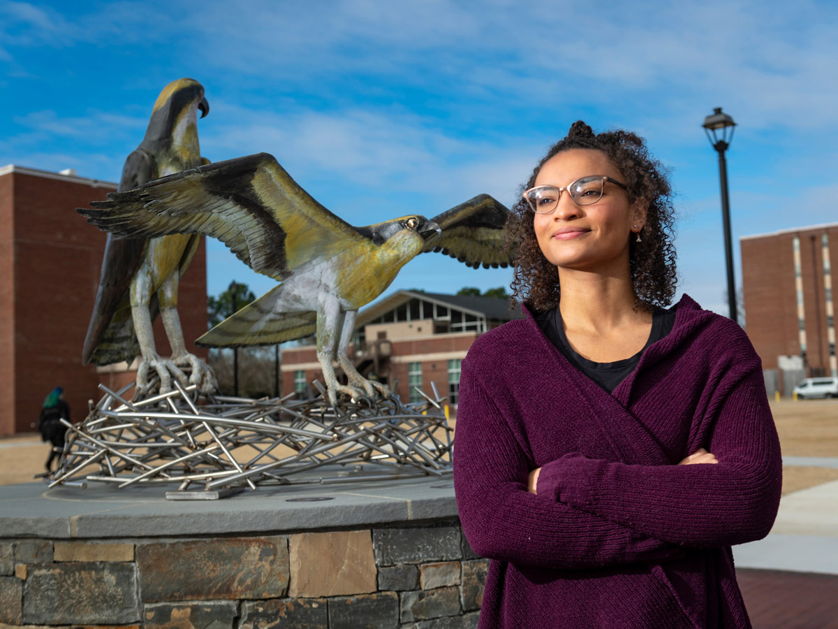 A student stands proudly in front of the Seahawk Statue